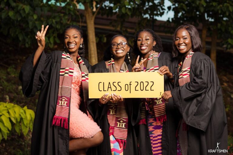 four dark girls smiling, in graduation gowns holding a 'Class of 2022' sign
