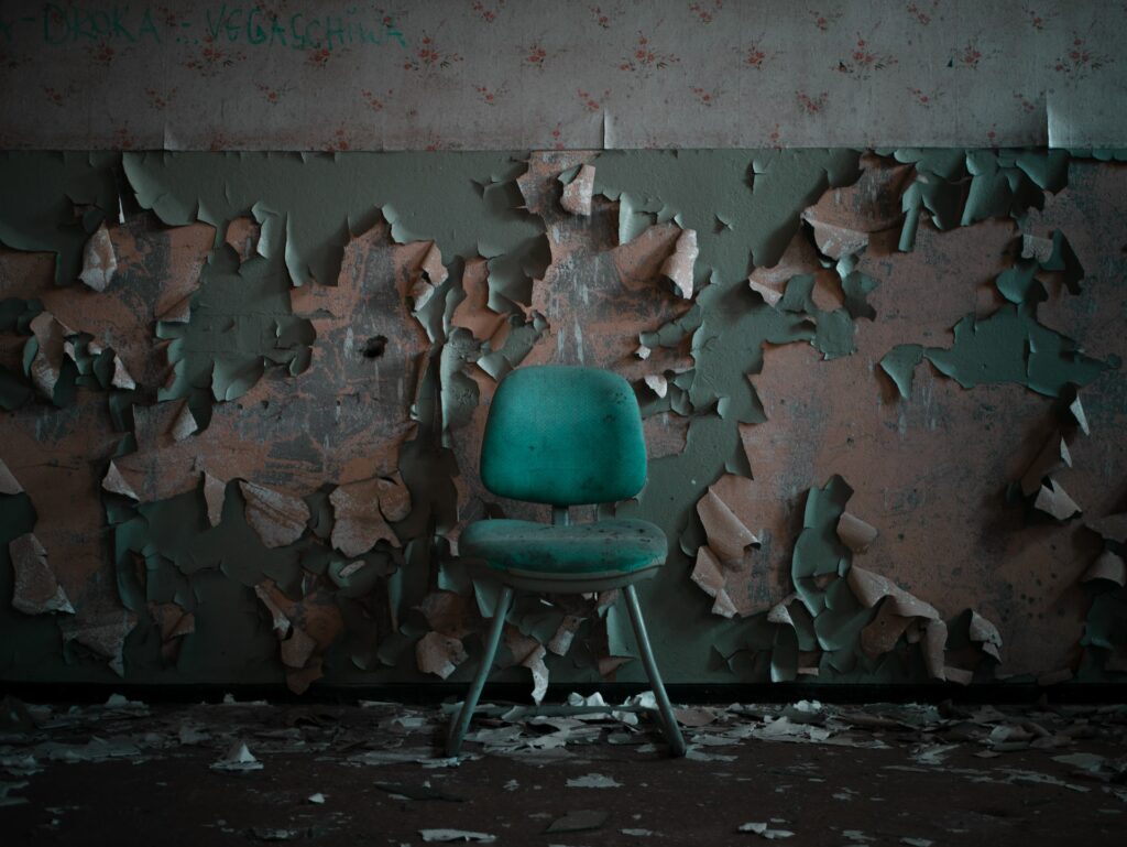 pain and suffering: peeling wall with a green chair infront of the wall